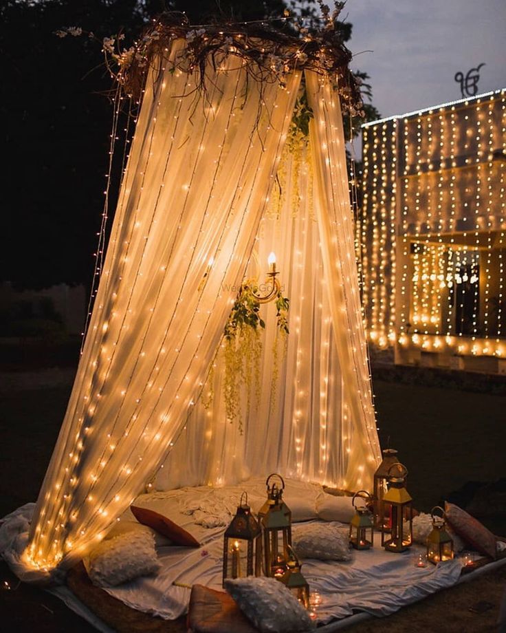 A cozy lighted tent with hanging string lights and soft drapes, creating an intimate outdoor space for a celebration.