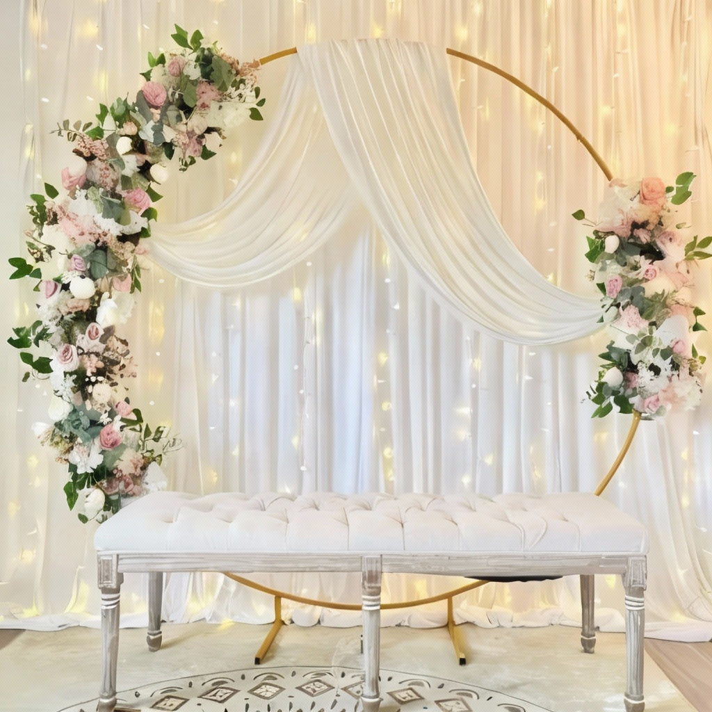 A beautifully decorated wedding arch with white drapes and floral arrangements, set against a backdrop of fairy lights.