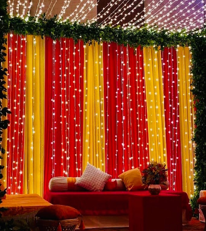 A beautiful wedding backdrop with red and yellow fabric drapes, sparkling string lights, and soft decorative touches, perfect for an elegant and festive Indian wedding setting.