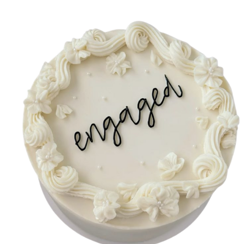 Engagement cake with white cream flowers, swirls, and Engaged message on top.