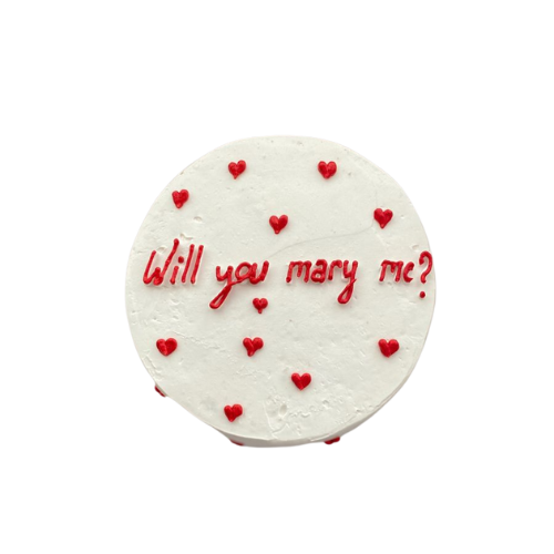 Engagement proposal cake with white icing, red hearts, and Will You Marry Me message.