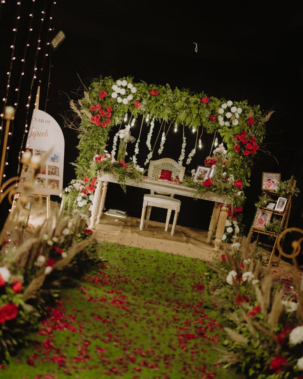 Photo booth with green floral arch, rustic wooden table, and floral decorations.