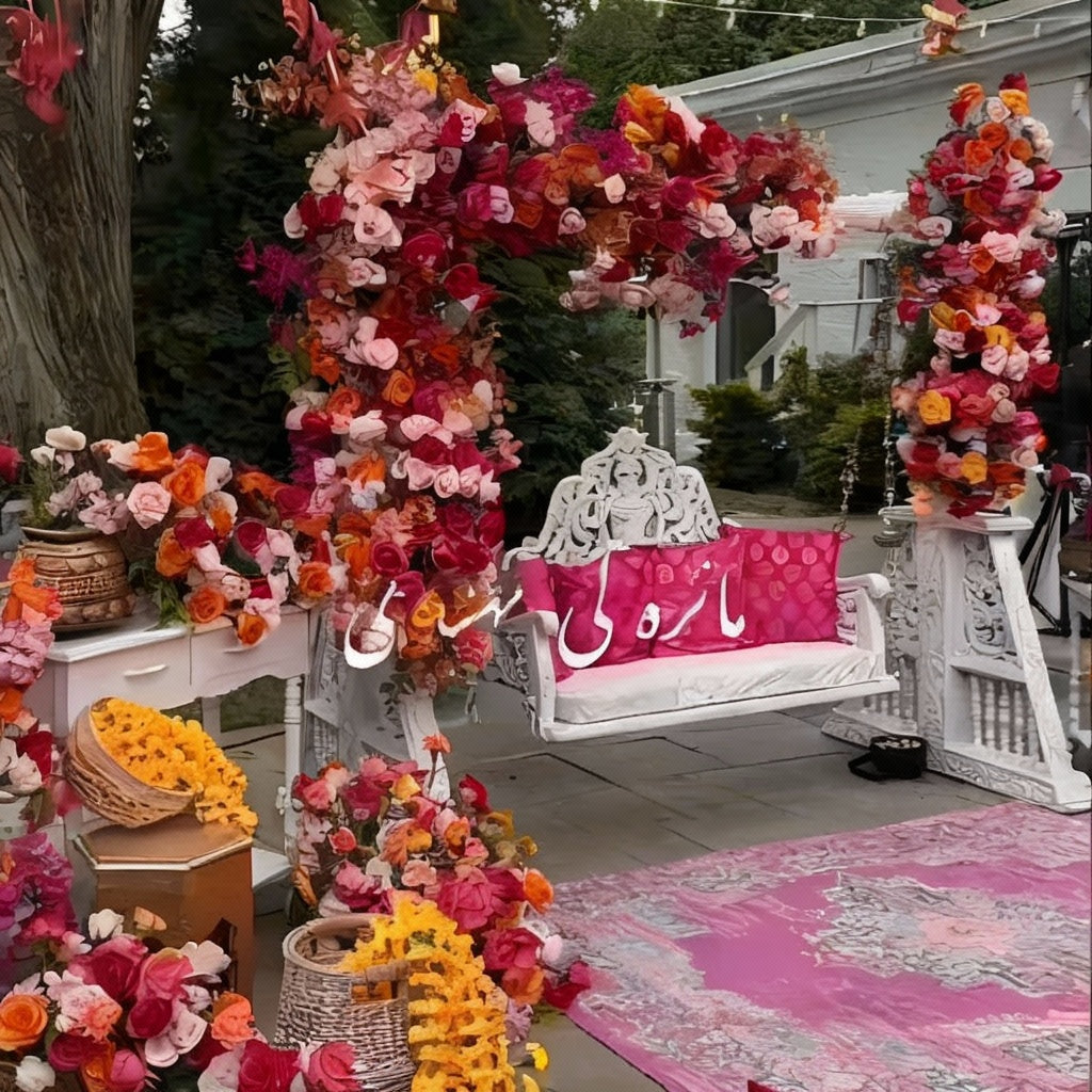 Outdoor Mehndi decor with a white swing, pink, red, and orange floral arrangements, marigold strings, and traditional props for a festive ambiance.