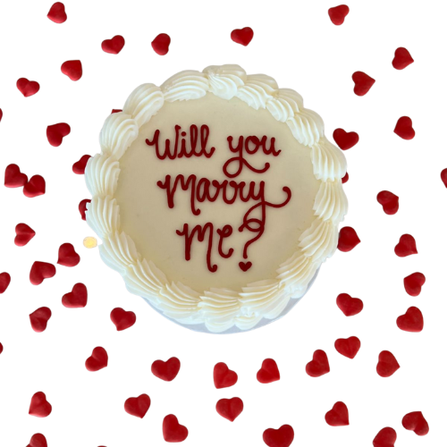 Proposal engagement cake with white cream frosting, red hearts, and Will You Marry Me message.