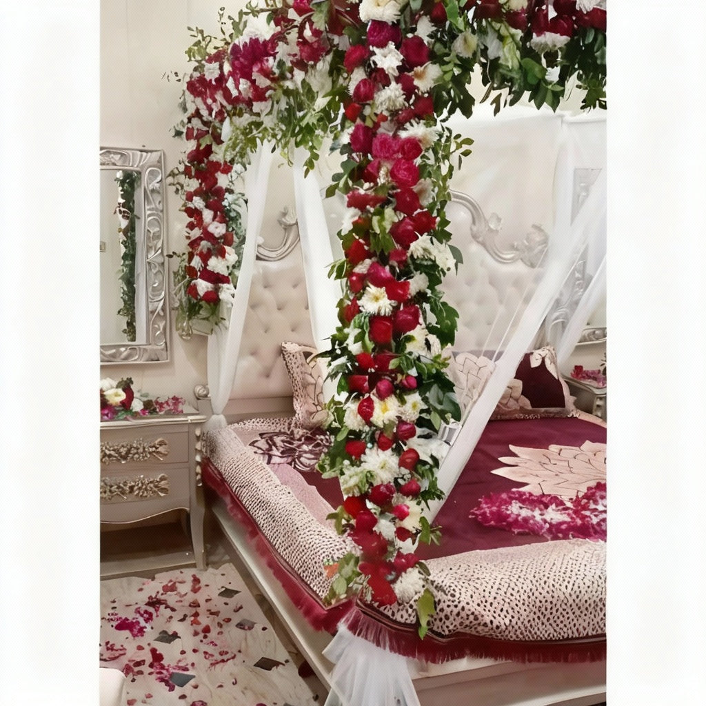 Romantic Flower Canopy Bed Decor with red and white flowers, green foliage, maroon and beige bedspread, and rose petals.