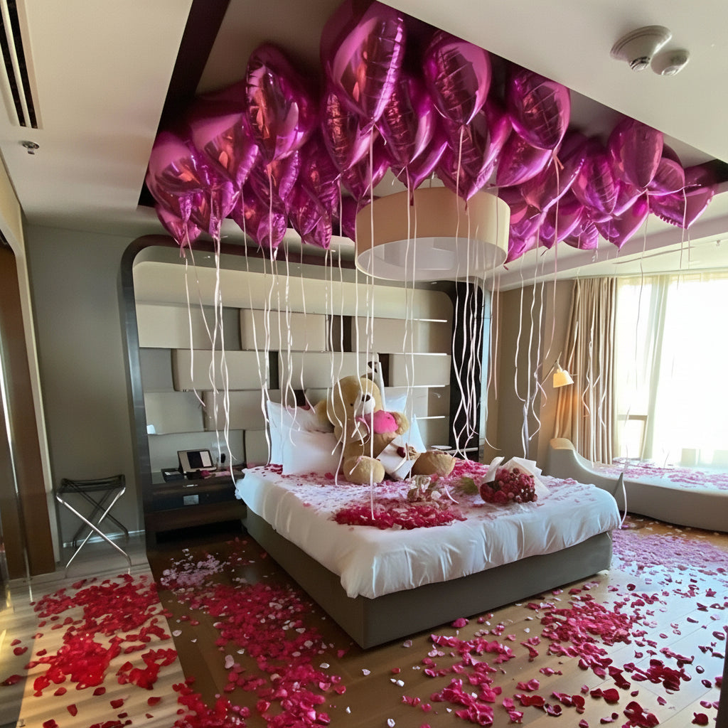 Romantic room decoration with pink rose petals, pink heart-shaped balloons, and a large teddy bear creating a dreamy and loving atmosphere.