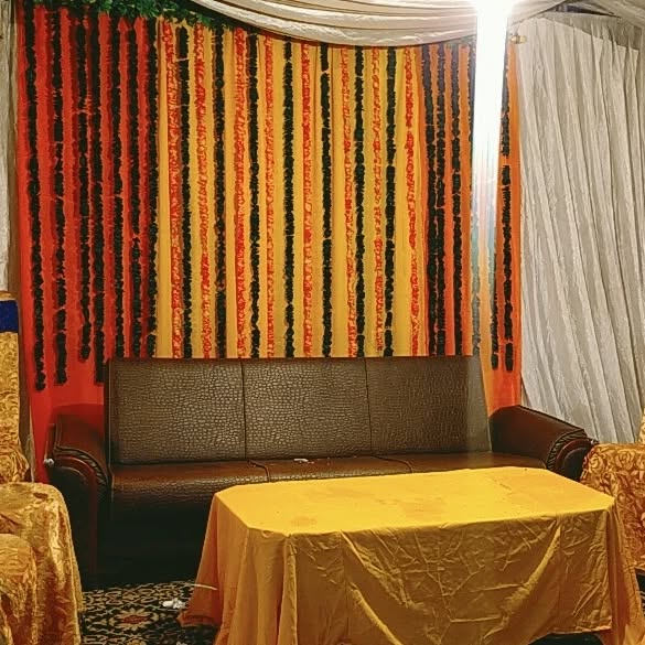 Bright yellow and red floral strings arranged as a backdrop with marigold and rose flowers for an event space, complete with a sofa and table in the foreground.