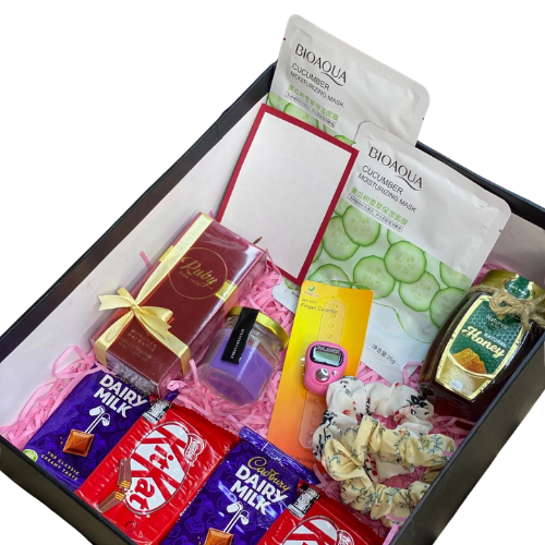 Wellness gift box with scented candle, Bioaqua sheet masks, Bonanza Ruby perfume, honey jar, chocolates, scrunchies, tasbih counter, and handwritten card.